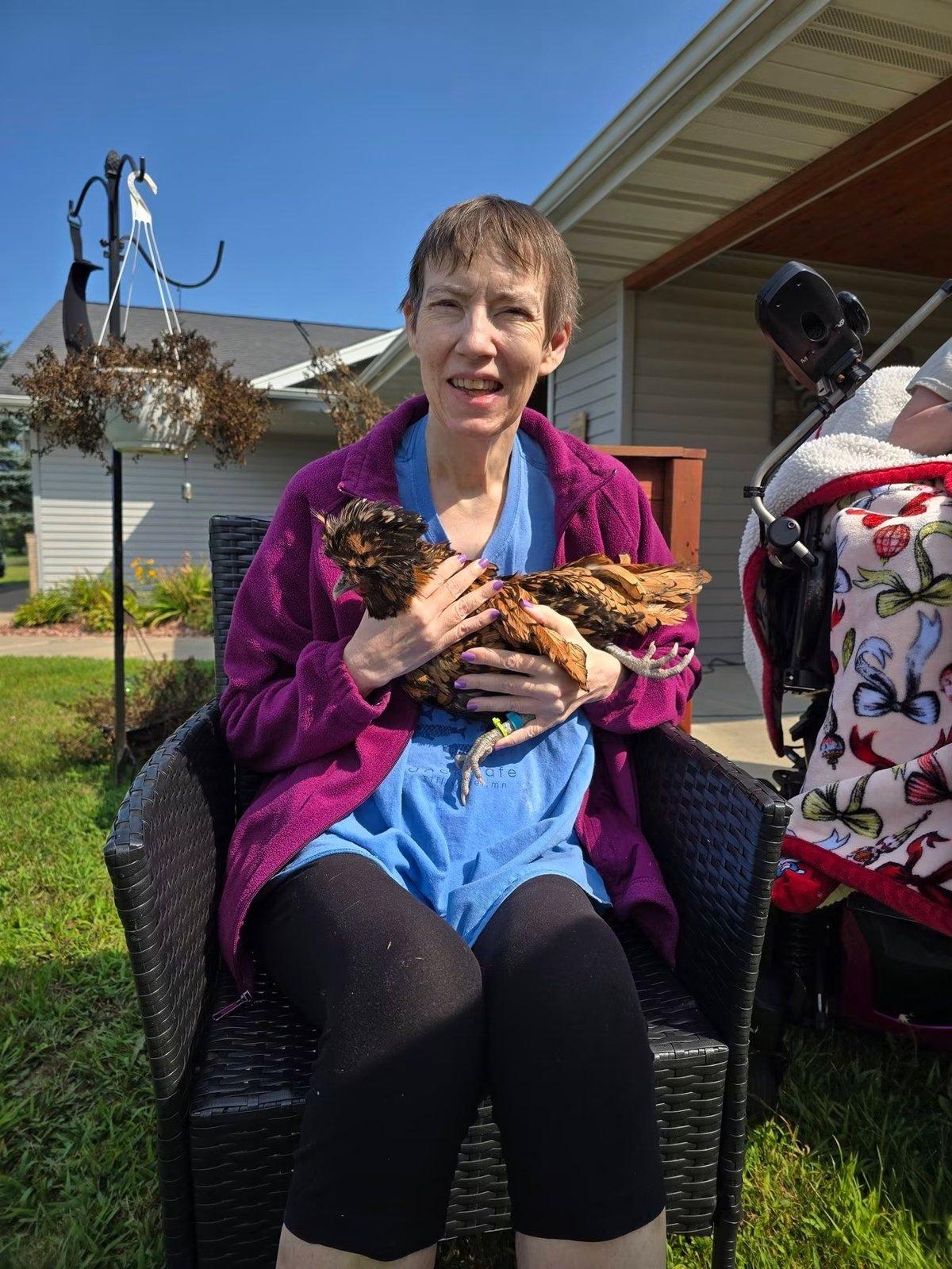 A woman seated outdoors cradles a chicken in her arms.