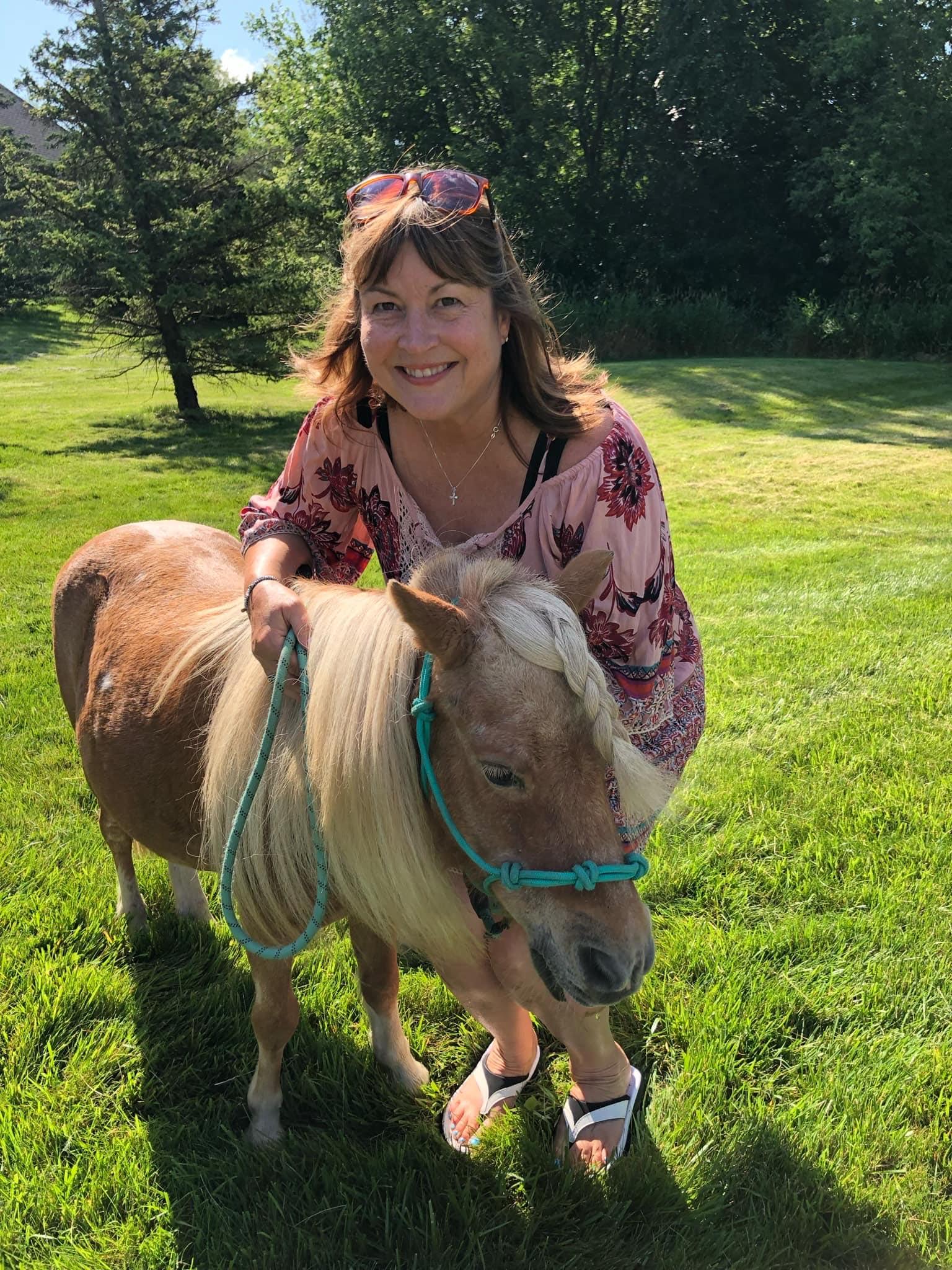 An adult smiling with a pony at a Pony Parties Express event