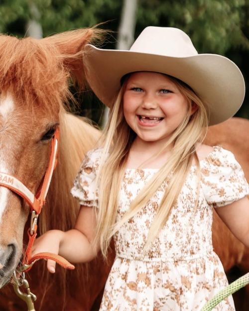 Bam Bam, a chestnut pony, standing beside a smiling young girl in a cowboy hat.