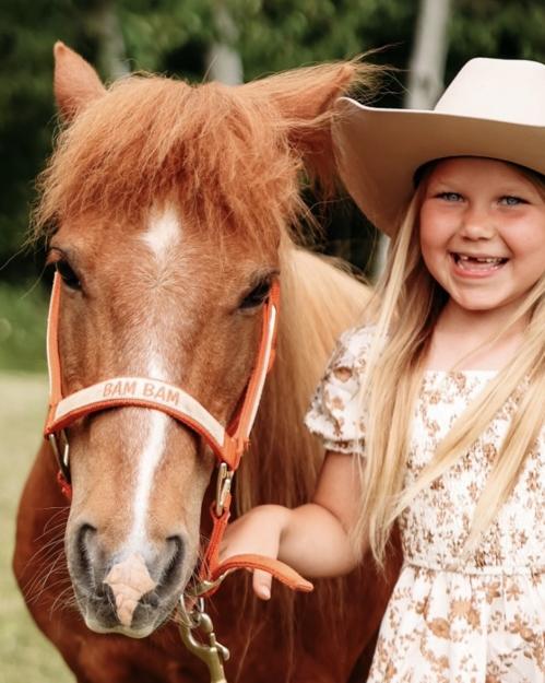 Bam Bam, a chestnut pony, standing beside a smiling young girl in a cowboy hat.