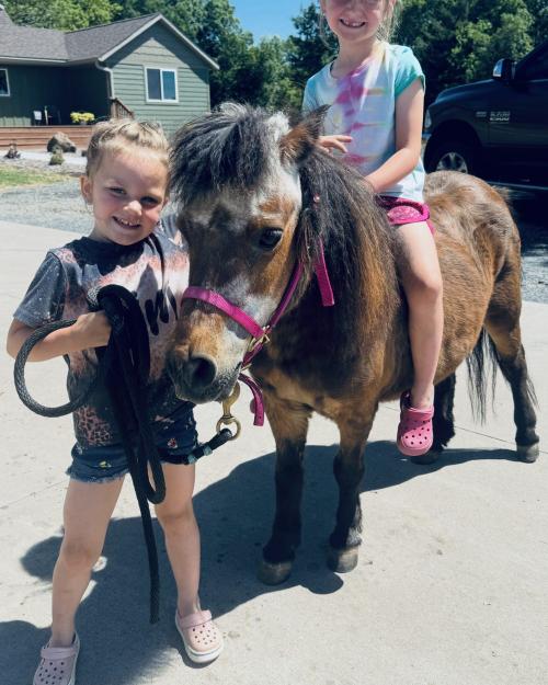 Belle, a brown and white pony, held by one girl while another rides bareback.