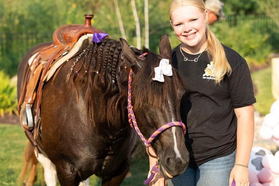 A handler with a pony wearing a braided mane and bows before a party