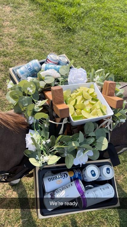 Top-down view of the saddle bar: a dish of cut limes between two boxes of cold cans, wrapped in eucalyptus and white flowers.