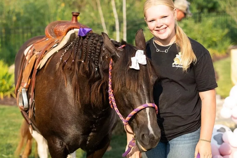 A handler with a pony wearing a braided mane and bows before a party