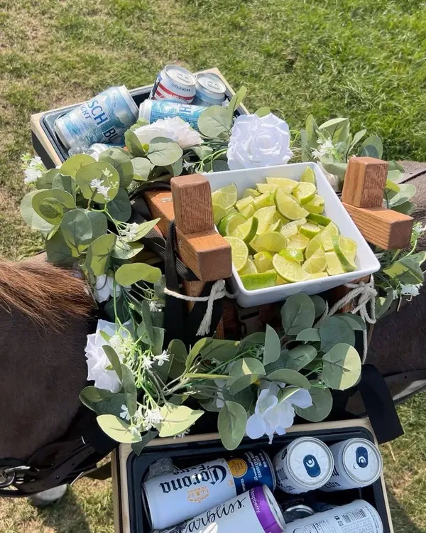 Top-down view of the saddle bar: a dish of cut limes between two boxes of cold cans, wrapped in eucalyptus and white flowers.