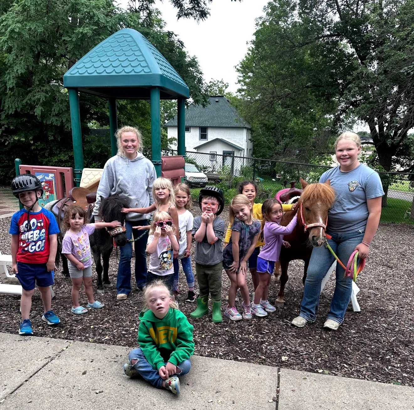 Two ponies visiting a playground with a group of children